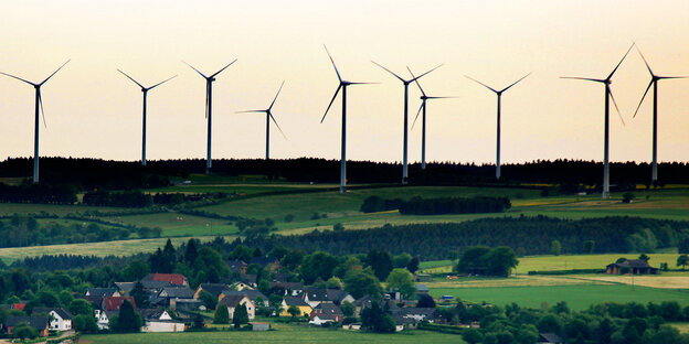 Ein Dorf am Berghang, darüber Windräder