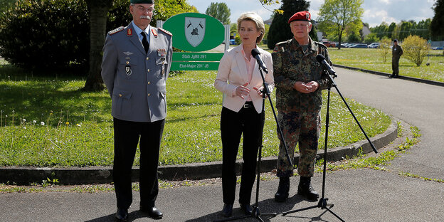 Verteidigungsministerin gerahmt von zwei Soldaten vor einem Mikro im Freien Verteidigungsministerin gerahmt von zwei Soldaten vor einem Mikro im Freien