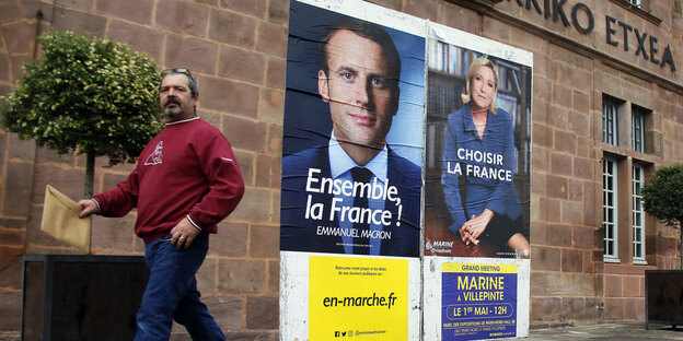 Zwei Wahlplakate mit den Konterfeis Macrons und Le Pens hängen nebeneinander, dahinter geht ein Mann Zwei Wahlplakate mit den Konterfeis Macrons und Le Pens hängen nebeneinander, dahinter geht ein Mann