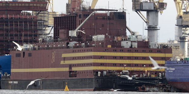 Ein großes Schiff in rotbraun mit beigen Streifen, dahinter Kräne Ein großes Schiff in rotbraun mit beigen Streifen, dahinter Kräne