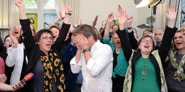 Robert Habeck schlägt sich bei der Wahlparty der Grünen in Kiel die Hände vors Gesicht, während um ihn herum alle jubeln Robert Habeck schlägt sich bei der Wahlparty der Grünen in Kiel die Hände vors Gesicht, während um ihn herum alle jubeln