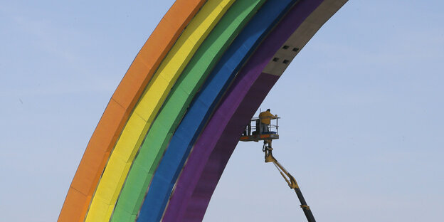 Ein Mann auf einer Hebebühne im schon in Regenbogenfarben bemalten Torbogen Ein Mann auf einer Hebebühne im schon in Regenbogenfarben bemalten Torbogen