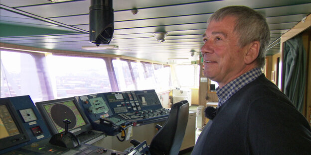 Ein Mann mit grauen Haaren steht auf der Brücke eines Schiffes