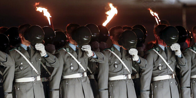 Soldaten mit Fackeln in Reih und Glied halten sich Helme vor das Gesicht Soldaten mit Fackeln in Reih und Glied halten sich Helme vor das Gesicht