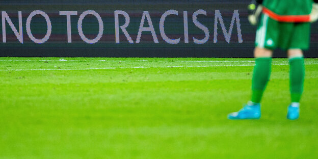Ein Fußballspieler, dessen Oberkörper man nicht sieht, auf einem Fußballplatz vor einer Bande mit der Aufschrift "No to Racism". Ein Fußballspieler, dessen Oberkörper man nicht sieht, auf einem Fußballplatz vor einer Bande mit der Aufschrift "No to Racism".