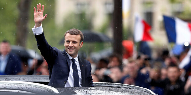 Macron winkt aus dem Schiebedach eines Autos heraus Macron winkt aus dem Schiebedach eines Autos heraus