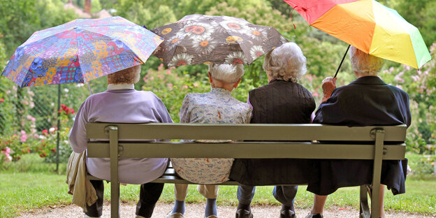 Seniorinnen sitzen auf einer Bank und halten bunte Regenschirme in den Händen Seniorinnen sitzen auf einer Bank und halten bunte Regenschirme in den Händen