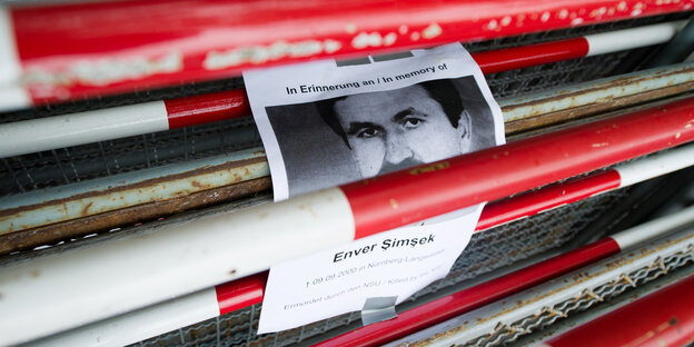 Ein Schild mit der Aufschrift "In Erinnerung an Enver Simsek - 9.9.2000 ermordet durch den NSU" klebt zwischen Absperrgittern am Oberlandesgericht in München Ein Schild mit der Aufschrift "In Erinnerung an Enver Simsek - 9.9.2000 ermordet durch den NSU" klebt zwischen Absperrgittern am Oberlandesgericht in München
