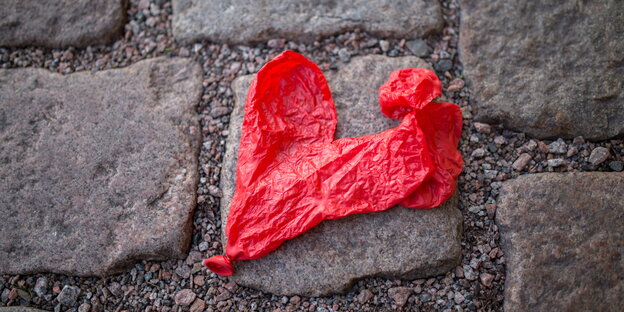 Ein zerplatzter roter Luftballon in Herzform liegt auf dem Boden Ein zerplatzter roter Luftballon in Herzform liegt auf dem Boden