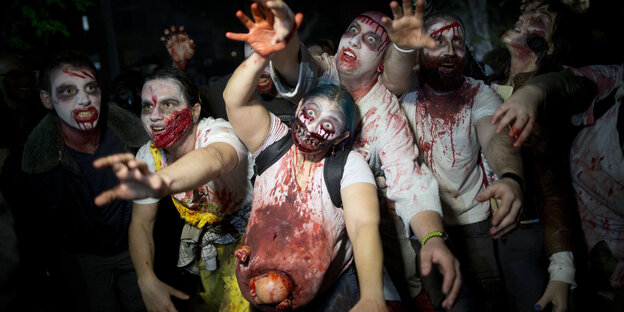 Eine Gruppe Menschen hat sich als blutverschmierte Zombies verkleidet und reckt die Arme in die Gegend Eine Gruppe Menschen hat sich als blutverschmierte Zombies verkleidet und reckt die Arme in die Gegend