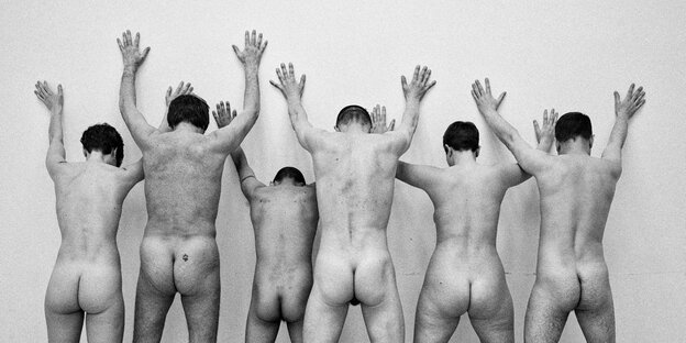 Sechs nackte Menschen stehen mit dem Gesicht zur Wand. Sie haben ihre Hände erhoben Sechs nackte Menschen stehen mit dem Gesicht zur Wand. Sie haben ihre Hände erhoben