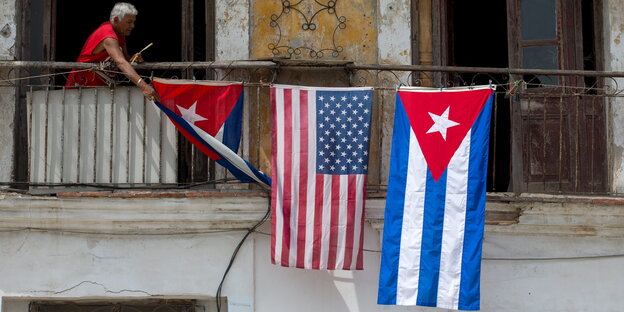 Ein Mann hängt US-amerikanische und kubanische Flaggen an einem Haus in Havana Ein Mann hängt US-amerikanische und kubanische Flaggen an einem Haus in Havana