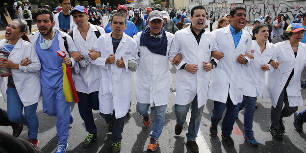 Ärztinnen und Ärzte marschieren eingehakt in einer Reihe bei einer Demo in Caracas