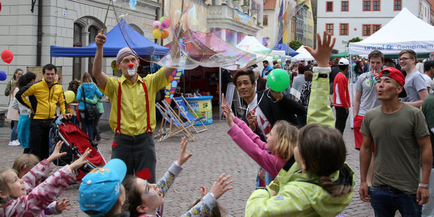 Ein Clownsperformance auf einem Marktplatz. Kinder schauen zu Ein Clownsperformance auf einem Marktplatz. Kinder schauen zu