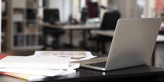 Ein Laptop und ein Stapel Bücher auf einem Schreibtisch in einem Büroraum