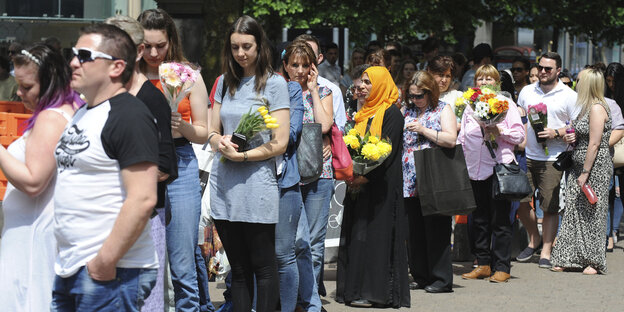 Menschen stehen in einer langen Schlange, sie halten Blumen in ihren Händen Menschen stehen in einer langen Schlange, sie halten Blumen in ihren Händen