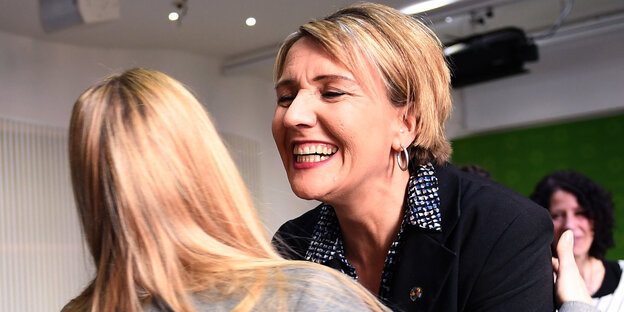 Eine Frau mit kurzen blonden Haaren umarmt eine andere Frau mit langen blonden Haaren Eine Frau mit kurzen blonden Haaren umarmt eine andere Frau mit langen blonden Haaren