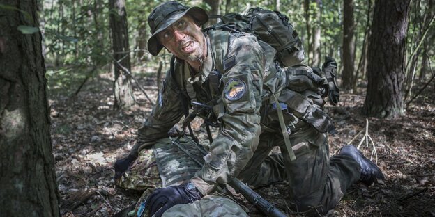 Ein Mann in Flecktarn kniet in einem Wald Ein Mann in Flecktarn kniet in einem Wald