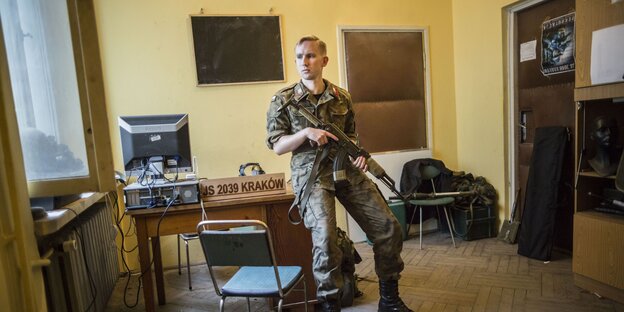 Ein uniformierter Mann mit Sturmgewehr lehnt an einem Schreibtisch Ein uniformierter Mann mit Sturmgewehr lehnt an einem Schreibtisch