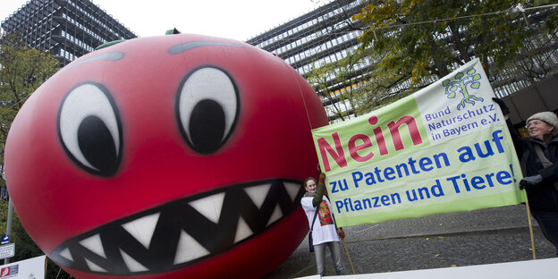 Eine aufblasbare Riesentomate auf einer Demonstration, daneben Transparent gegen Patente auf Saatgut. Eine aufblasbare Riesentomate auf einer Demonstration, daneben Transparent gegen Patente auf Saatgut.