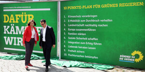 Eine Frau und ein Mann stehen vor Plakatwänden mit dem Zehn-Punkte-Plan der Grünen