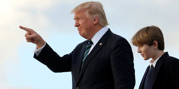 Ein Junge und ein älterer Mann stehen nebeneinander, der Mann zeigt mit seinem Finger auf die Sonne Ein Junge und ein älterer Mann stehen nebeneinander, der Mann zeigt mit seinem Finger auf die Sonne