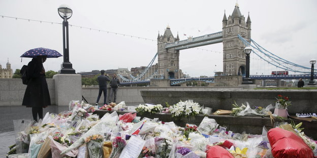 Eine Frau mit Regenschirm steht vor den Blumen, die für die Opfer des Anschlags vor der London Bridge niedergelegt sind