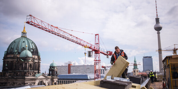 Ein Bauarbeiter arbeitet auf dem Dach, im Hintergrund Berliner Dom, Fernsehturm und ein Baukran Ein Bauarbeiter arbeitet auf dem Dach, im Hintergrund Berliner Dom, Fernsehturm und ein Baukran