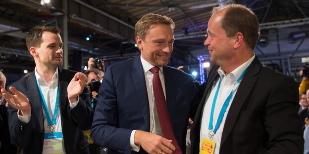 Drei Männer stehen nebeneinander, einer klatscht in die Hände Drei Männer stehen nebeneinander, einer klatscht in die Hände