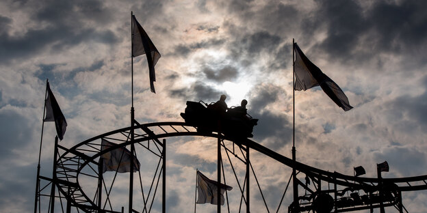 Zwei Personen fahren bei Sonnenuntergang mit dramatisch bewölktem Himmel auf einer Achterbahn.