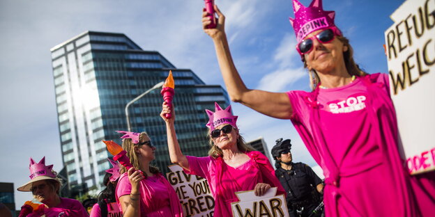 Frauen in pinkfarbenen Kleidern halten pinkfarbene Fackelattrappen in der Hand Frauen in pinkfarbenen Kleidern halten pinkfarbene Fackelattrappen in der Hand