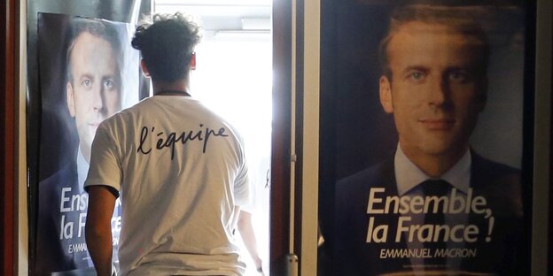 Ein Mann geht neben einem Plakat von Macron durch eine Tür ins Licht Ein Mann geht neben einem Plakat von Macron durch eine Tür ins Licht