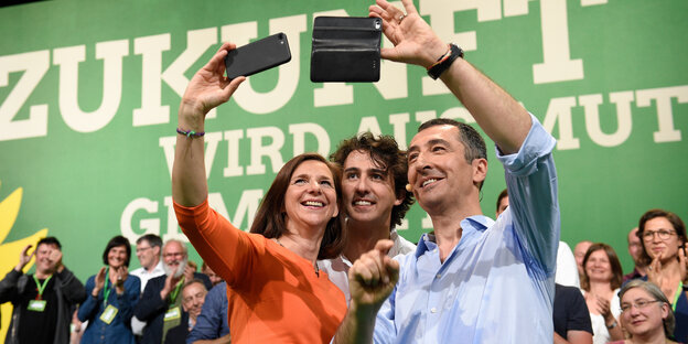 Drei Menschen machen ein Selfie vor der Kulisse des Grünen-Parteitags Drei Menschen machen ein Selfie vor der Kulisse des Grünen-Parteitags
