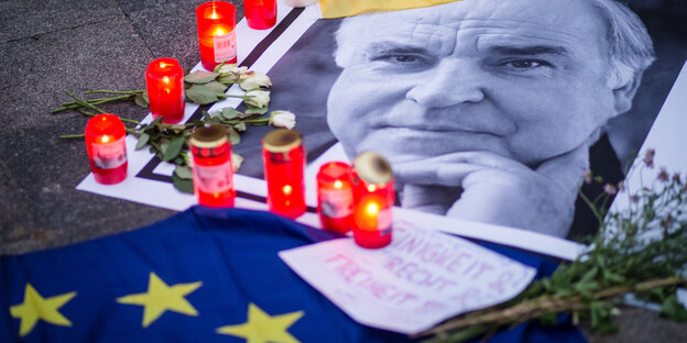 Eine Schwarzweiß-Aufnahme Helmut Kohls zwischen Kerzen, Blumen und einer Europaflagge Eine Schwarzweiß-Aufnahme Helmut Kohls zwischen Kerzen, Blumen und einer Europaflagge