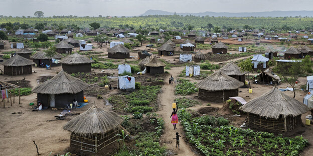 Häuser mit Strohdach stehen in einer idyllischen Landschaft. Dazwischen provisorische Zelthütten der UNHCR Häuser mit Strohdach stehen in einer idyllischen Landschaft. Dazwischen provisorische Zelthütten der UNHCR