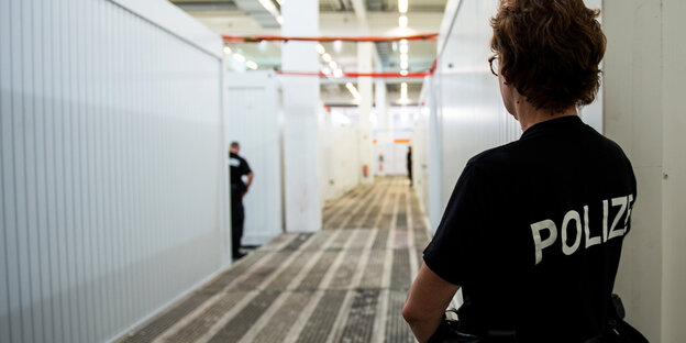 Personen besichtigen Container, im Vordergrund ein Polizist Personen besichtigen Container, im Vordergrund ein Polizist