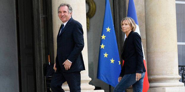 Ein Mann und eine Frau gehen eine Treppe hoch, im Hintergrund stehen eine EU- und eine Frankreich-Fahne Ein Mann und eine Frau gehen eine Treppe hoch, im Hintergrund stehen eine EU- und eine Frankreich-Fahne