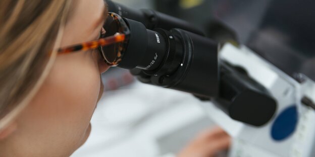 eine Frau mit Brille schaut durch ein Mikroskop eine Frau mit Brille schaut durch ein Mikroskop