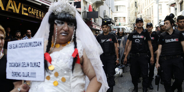 ein LGBTI-Community-Mitglied im Hochzeitskleid und mit Protestschild vor einer Reihe von Polizisten ein LGBTI-Community-Mitglied im Hochzeitskleid und mit Protestschild vor einer Reihe von Polizisten