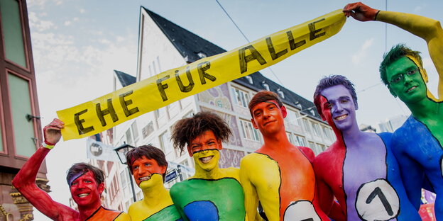 Bunt angemalte Männer halten ein Banner auf dem steht „Ehe für alle“