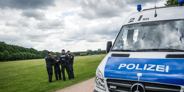 Polizisten auf einer Wiese, im Vordergrund ein Polizeifahrzeug Polizisten auf einer Wiese, im Vordergrund ein Polizeifahrzeug