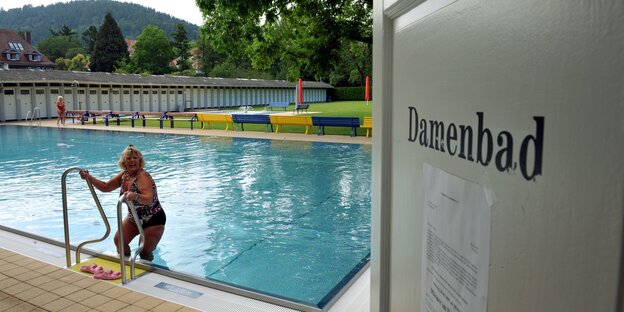 Eine Frau steigt aus einem Freibad-Becken, auf einer Tür daneben steht "Damenbad"