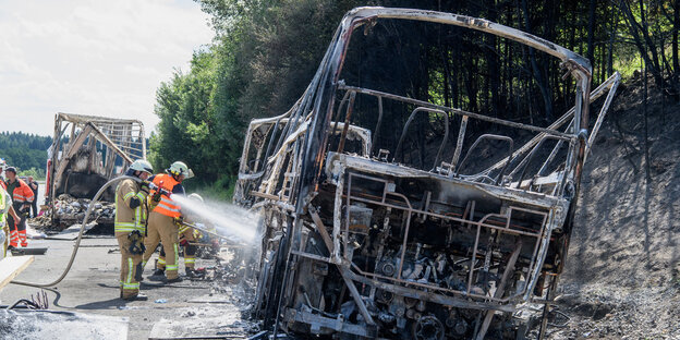 Feuerwehrleute löschen Brandreste an einem Autowrack Feuerwehrleute löschen Brandreste an einem Autowrack