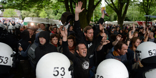 Polizisten mit weißen Helmen kesseln eine Gruppe Demonstranten unter einem Baum ein