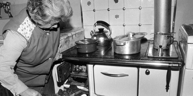 Eine Hausfrau schiebt mit einer Schaufel neue Kohle in ihren Ofen nach. Schwarzweiß-Bild von 1979. Eine Hausfrau schiebt mit einer Schaufel neue Kohle in ihren Ofen nach. Schwarzweiß-Bild von 1979.