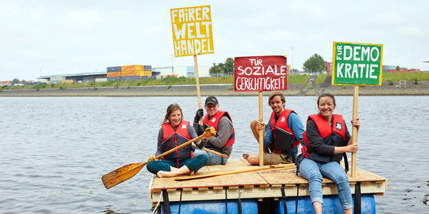 Vier Menschen auf einem Fluss. Sie halten Schilder in die Höhe, auf denen "soziale Gerechtigkeit" und "Demokratie" steht Vier Menschen auf einem Fluss. Sie halten Schilder in die Höhe, auf denen "soziale Gerechtigkeit" und "Demokratie" steht