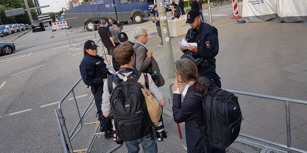 Menschen stehen zwischen Absperrgittern und werden von einem Polizisten kontrolliert Menschen stehen zwischen Absperrgittern und werden von einem Polizisten kontrolliert