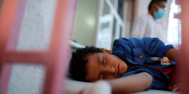 Ein Junge schläft auf einem Krankenbett. Hinter seinem Bett läuft ein Arzt entlang Ein Junge schläft auf einem Krankenbett. Hinter seinem Bett läuft ein Arzt entlang