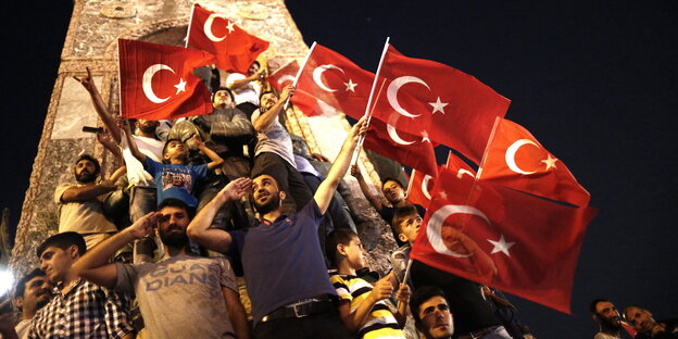 Männer halten türkische Flaggen vor einem Monument in die Höhe Männer halten türkische Flaggen vor einem Monument in die Höhe