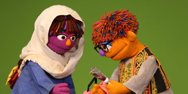 Die beiden Handpuppen Sari und Sirak betrachten gemeinsam einen Gegenstand, den Sirak in der Hand hält. Die beiden Handpuppen Sari und Sirak betrachten gemeinsam einen Gegenstand, den Sirak in der Hand hält.